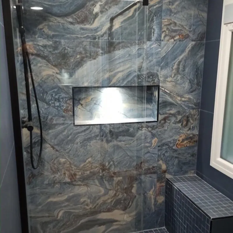 Ducha de obra con porcelánico efecto mármol azul, banco y grifería negra en una reforma de baño