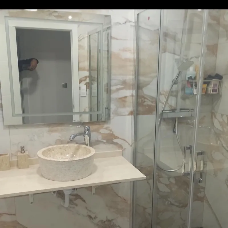 Baño con porcelánico efecto calacatta, lavabo de piedra sobre encimera y mampara de ducha corredera
