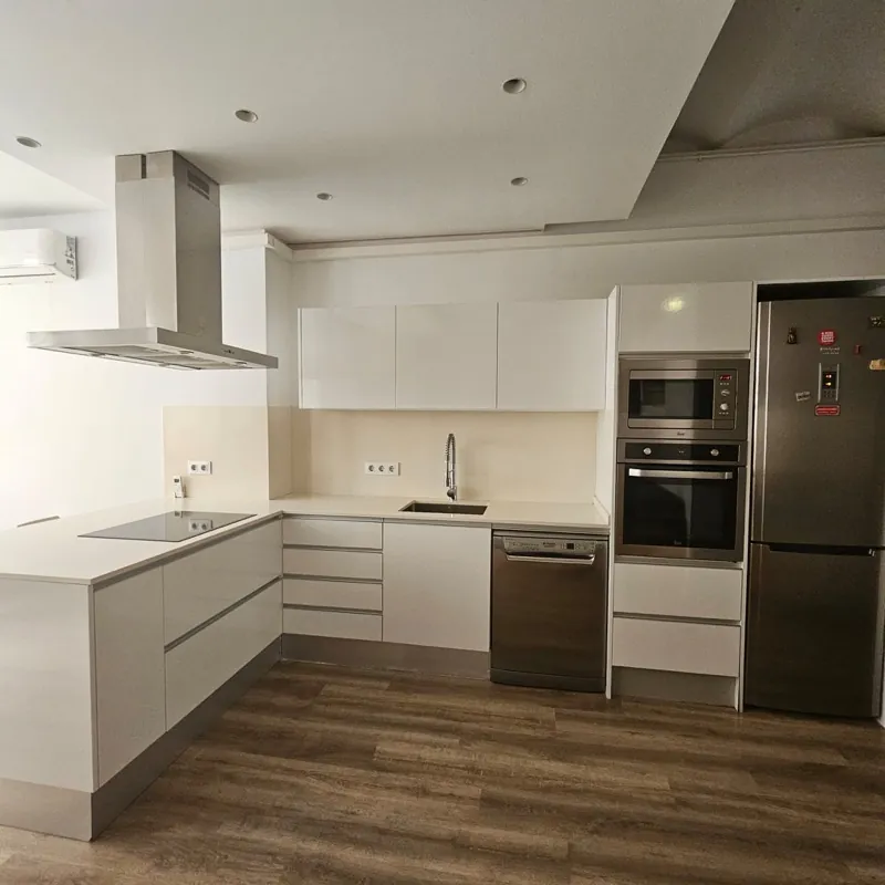 Cocina blanca en L con horno y microondas en columna, frente beige, campana de isla y suelo laminado
