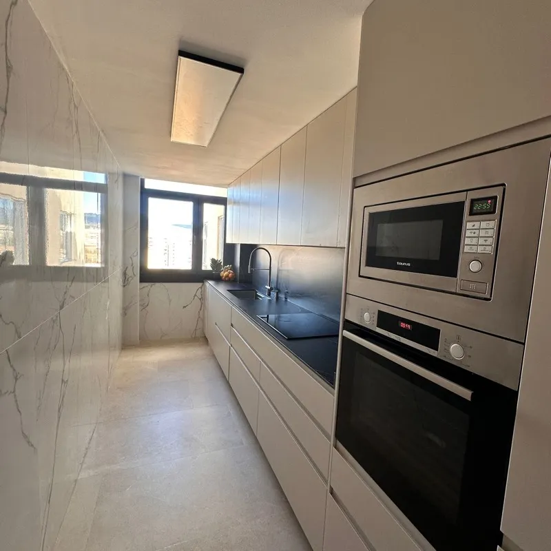Cocina en línea recién montada con muebles greige sin tirador, encimera negra, horno y microondas en columna