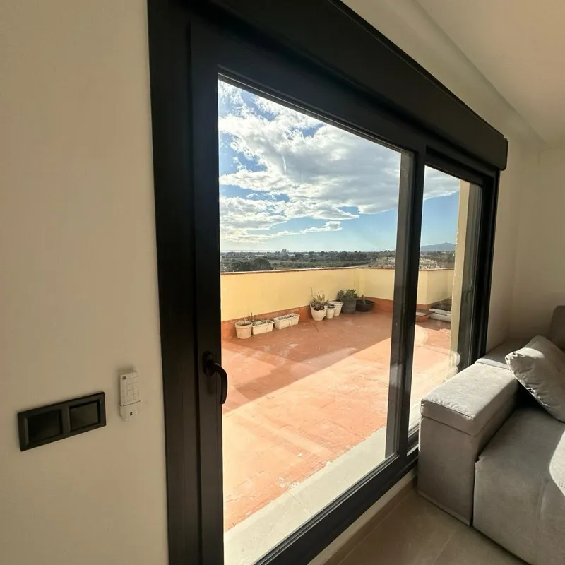Puerta corredera de aluminio negro de dos hojas con salida a un terrado, vista desde el salón