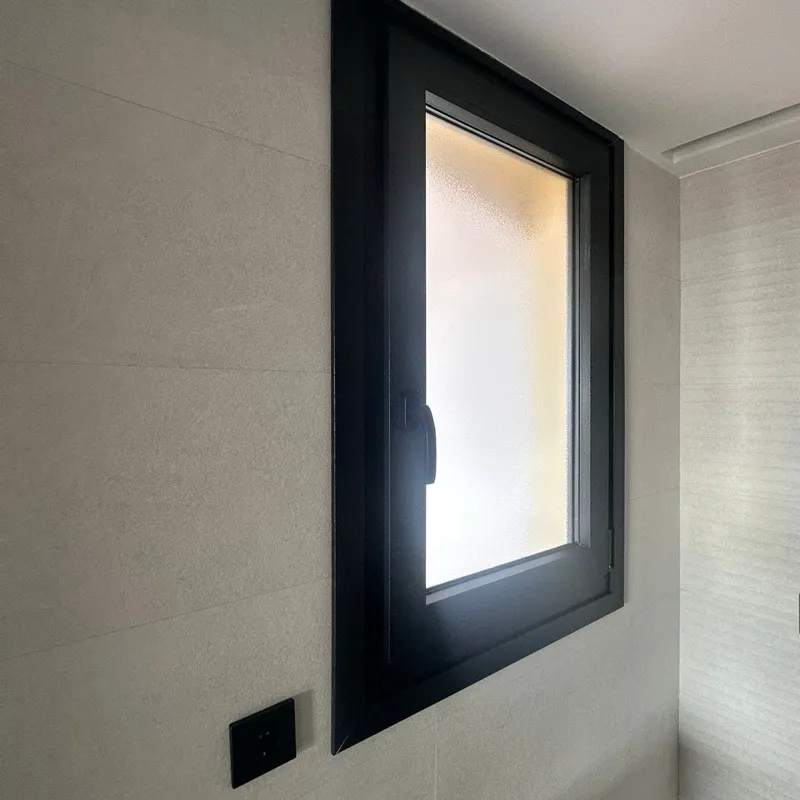 Ventana de aluminio negro con vidrio traslúcido en un baño de microcemento