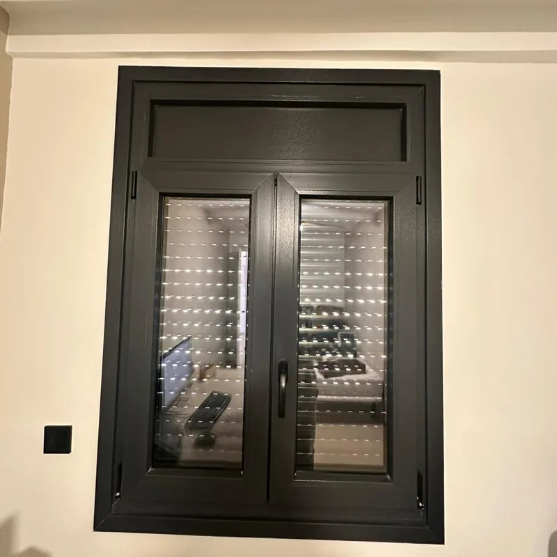Ventana de aluminio antracita con persiana de lamas bajada y cajón integrado en un dormitorio